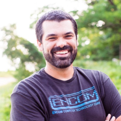 A person with a beard smiles outdoors, sporting a T-shirt emblazoned with "ENCOM COMPUTER TECHNOLOGY CORP," embodying the spirit of next-gen strategies.