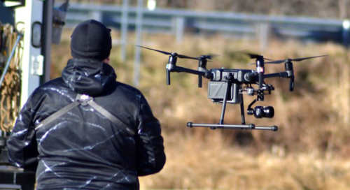 A person skillfully operates a drone equipped with a camera, flying it outdoors near a road, while remaining vigilant of domestic counter unmanned aircraft systems regulations.