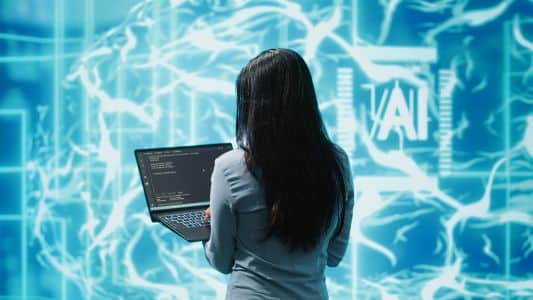 A woman with long dark hair uses a laptop displaying code, standing in front of a digital background with neural network graphics and the letters "AI," illustrating how Remote Browser Isolation can help protect against phishing attacks in 2026.