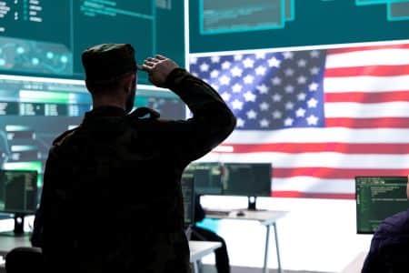 A soldier in uniform salutes in a command center equipped with advanced AV solutions and computer monitors, facing a large digital display of the American flag.