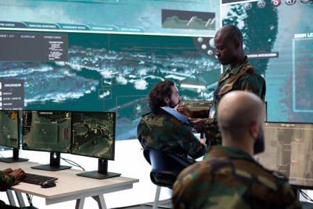 Military personnel in camouflage uniforms utilize advanced av solutions to monitor multiple surveillance screens and maps in a command center.